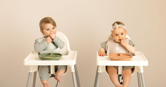 Two babies sitting in high chairs wearing KeaBabies silicone bibs while enjoying their meals.