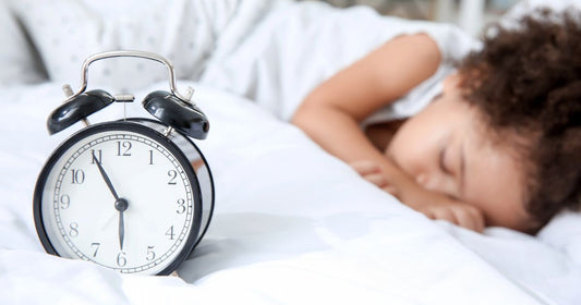 Toddler sleeping peacefully with an alarm clock beside her.