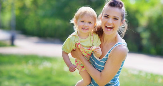 Smiling mother and baby playing together on a green lawn at a sunny park.