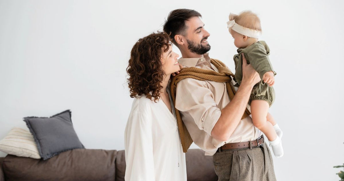 Cheerful young father holding his infant daughter while standing beside his curly-haired wife.