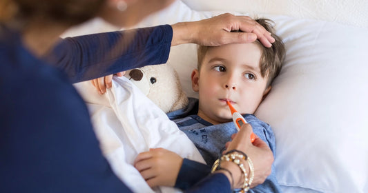 Sick child resting in bed while a parent checks their temperature.