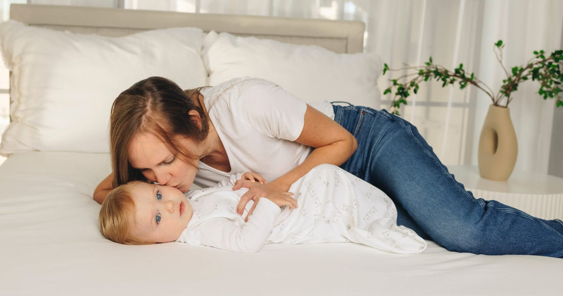 Mother lying on a bed beside her baby wearing a sleep sack during a quiet bonding moment before bedtime.
