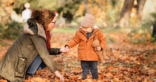 Mom and baby wearing warm snuggly clothes while playing outdoors with fallen autumn leaves.