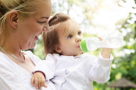 A mother carefully watching her baby drink water to stay hydrated in hot weather.