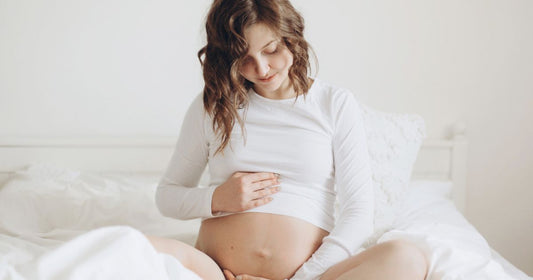 Expecting mother in a white top holding her baby bump and relaxing during pregnancy.