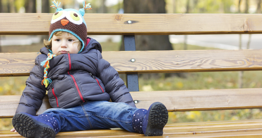 Toddler bundled up in warm layers, beanie, and cozy clothing sitting on a bench in cold weather.