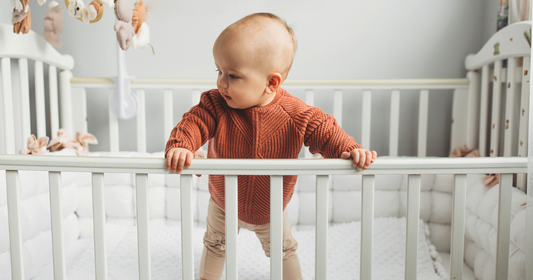 Adorable baby in a crib with a waterproof crib sheet for added comfort and protection.